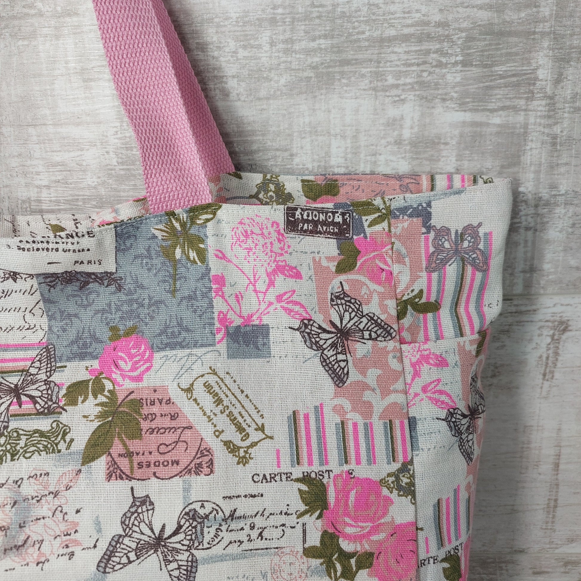 Close-up view of pink and grey rose and butterfly vintage print beach bag, showing outer pocket.