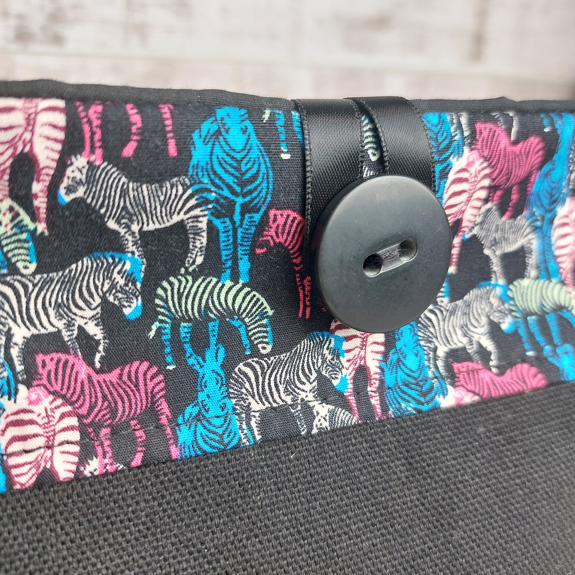 Close up of black button and ribbon fastening on a multicoloured zebra print button pouch by Olganna. 