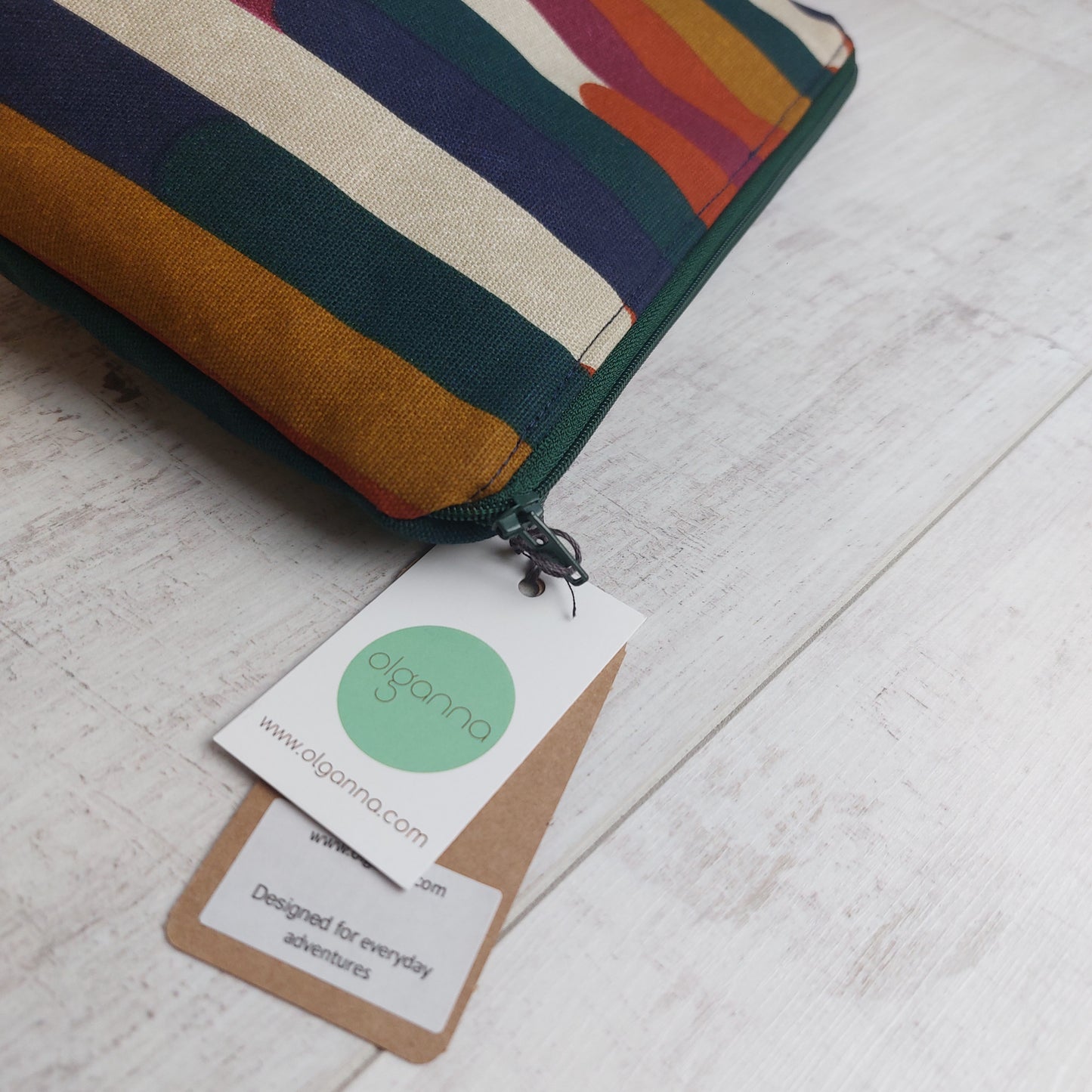 Toiletries zip bag in an autumn shades stripe pattern with green zip and a label saying 'Designed for everyday adventures www.olganna.com'