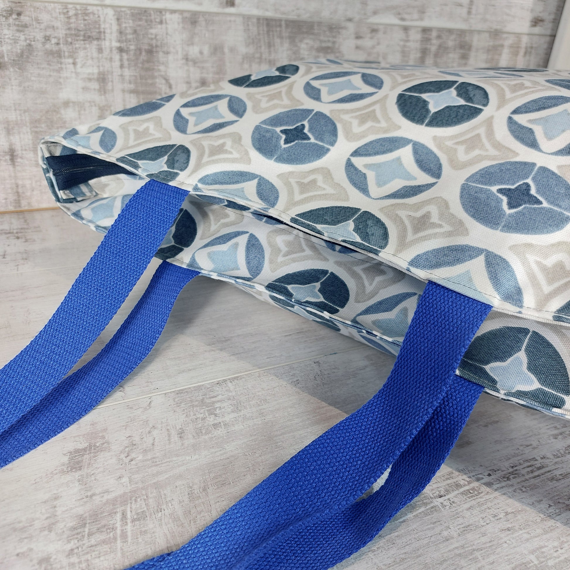 Blue Moroccan tile print beach bag, with deep-set zip closure, lying down. 