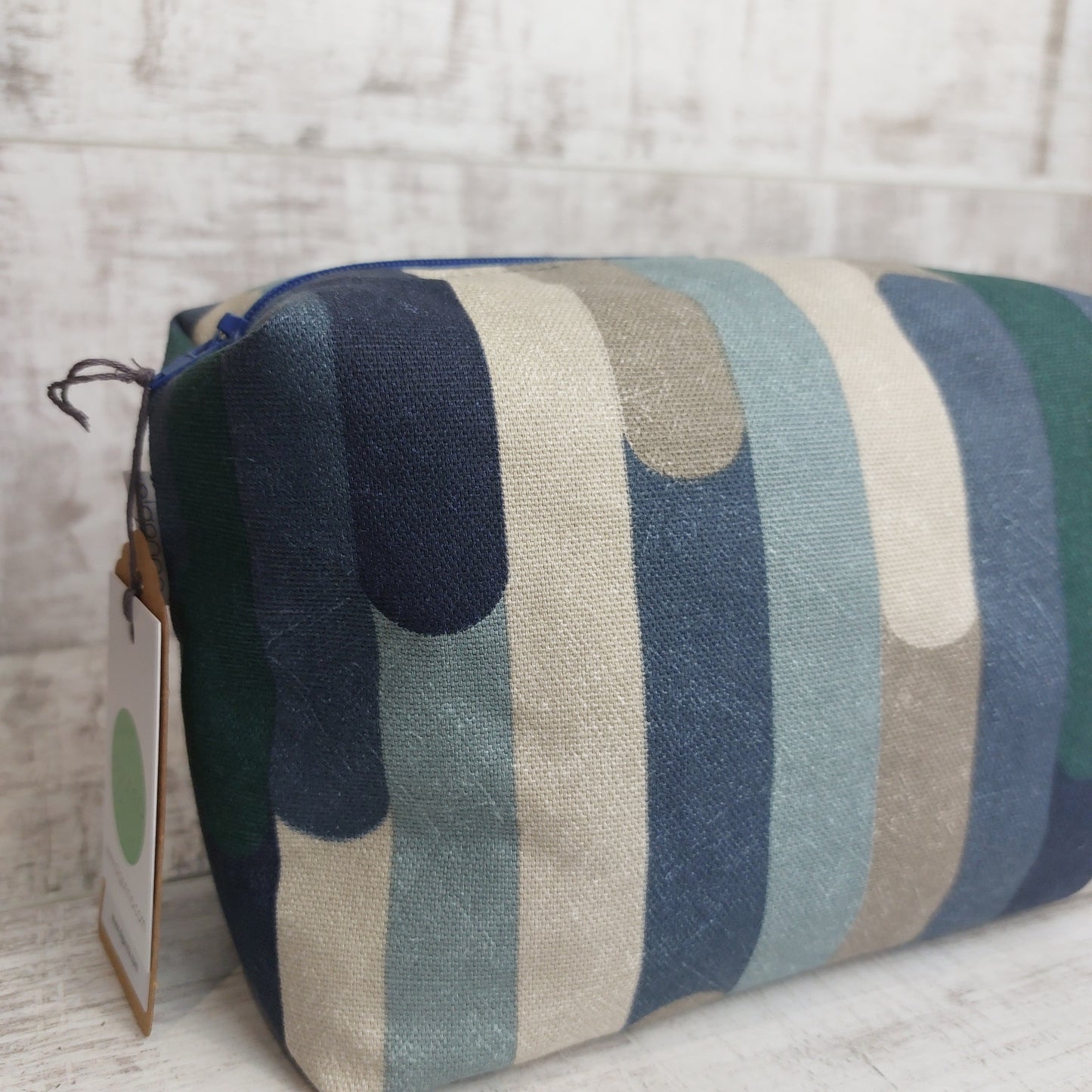 Closeup of boxy zip pouch in blue and winter tones stripe pattern with Olganna gift tag.