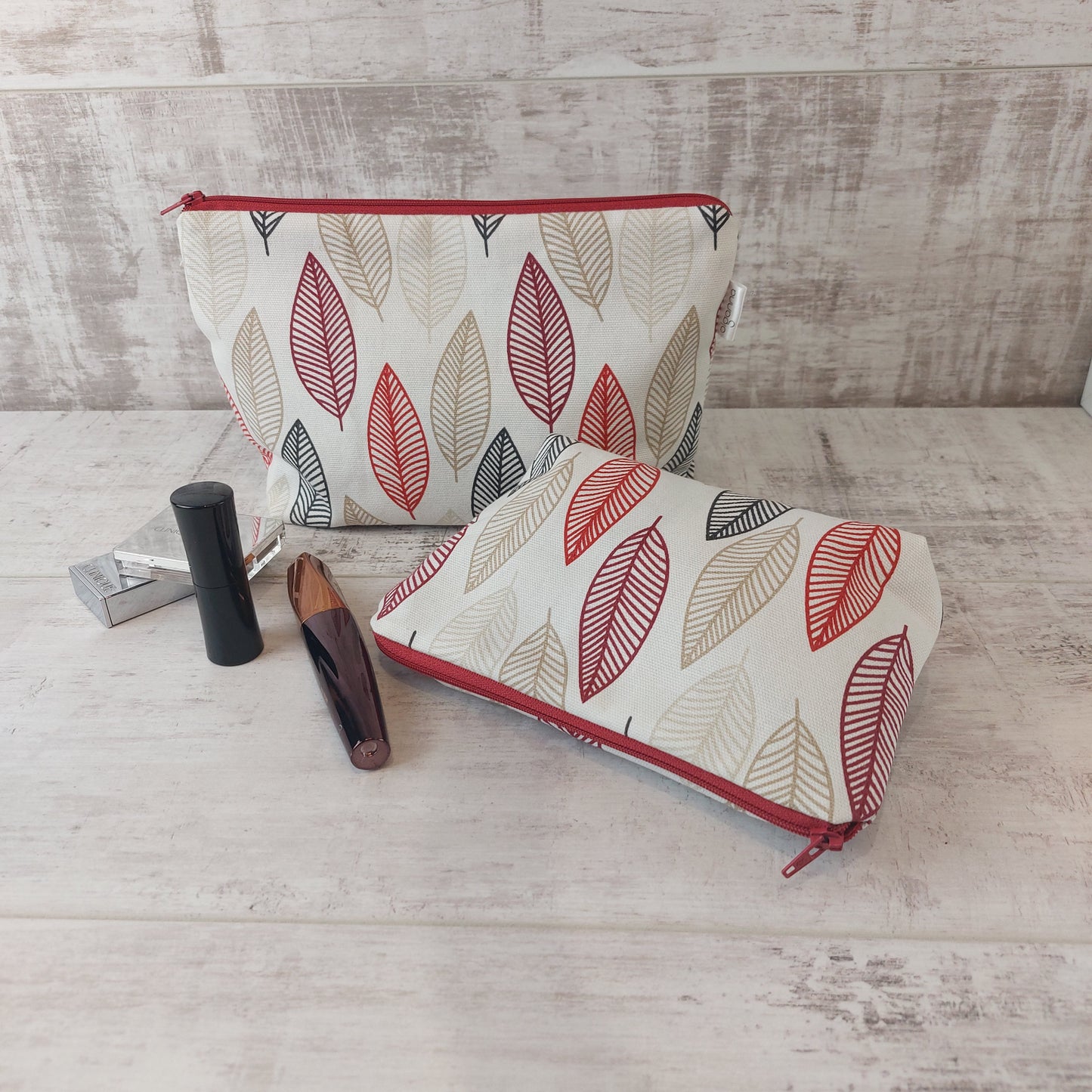 Small Scandi Autumn Leaves print pouch lying down with a larger pouch behind, pictured with beauty essentials, by Olganna.