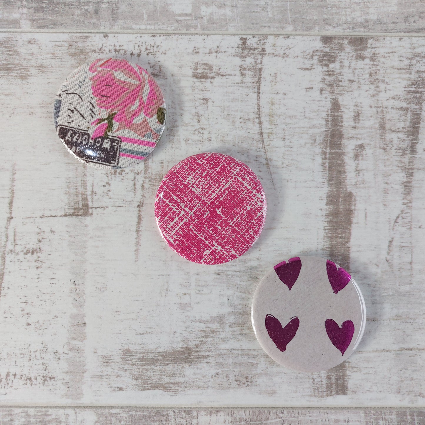 Three compact mirrors in a diagonal row with different designs featuring pink.