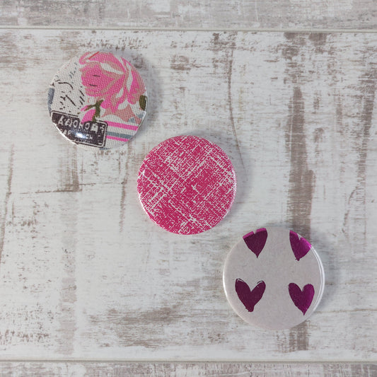 Three compact mirrors in a diagonal row with different designs featuring pink.