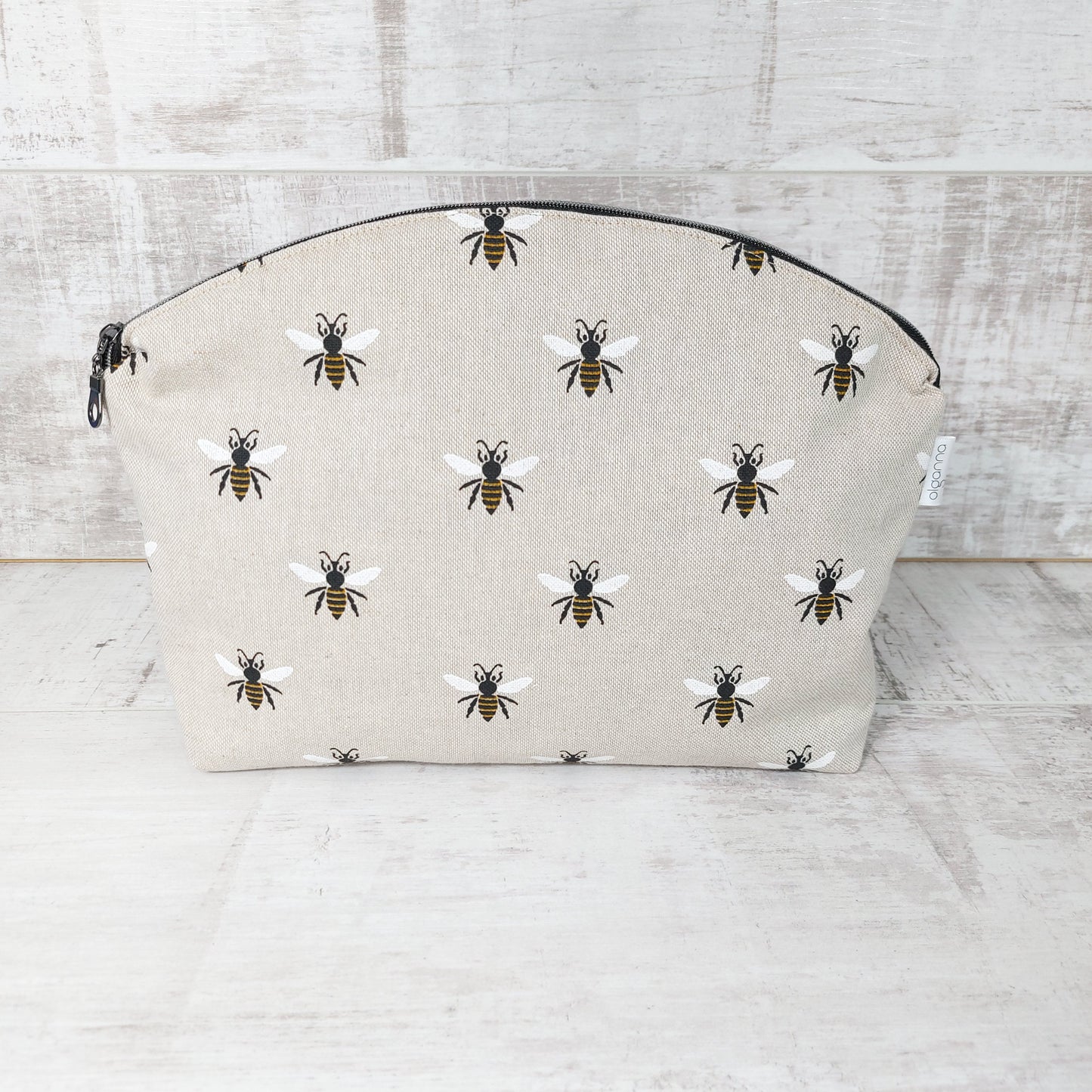 Large makeup bag with round zip opening standing upright with a zip fastening and repeat bee print on linen-look fabric.
