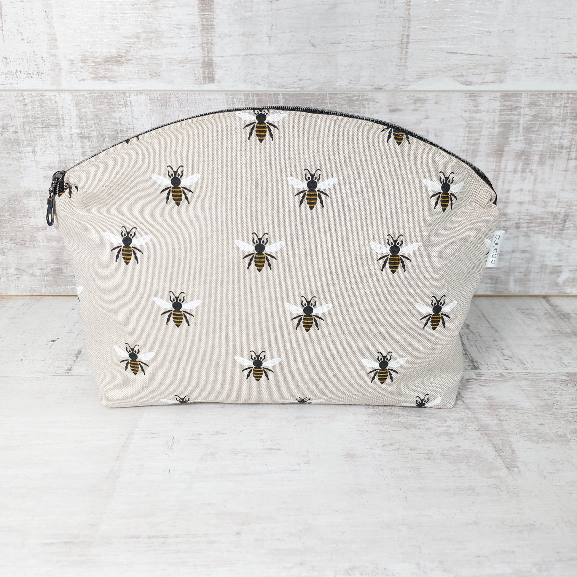 Large makeup bag with round zip opening standing upright with a zip fastening and repeat bee print on linen-look fabric.
