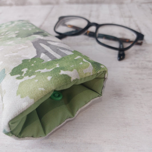 Closeup of green watercolour tree print glasses case with green lining and snap fastening, pictured with glasses.