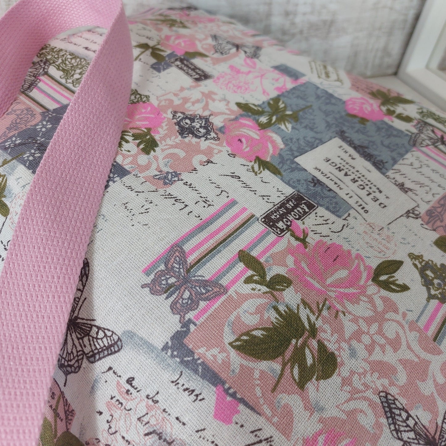 Close-up view of pink and grey vintage beach bag showing rose and butterfly print and pink strap.