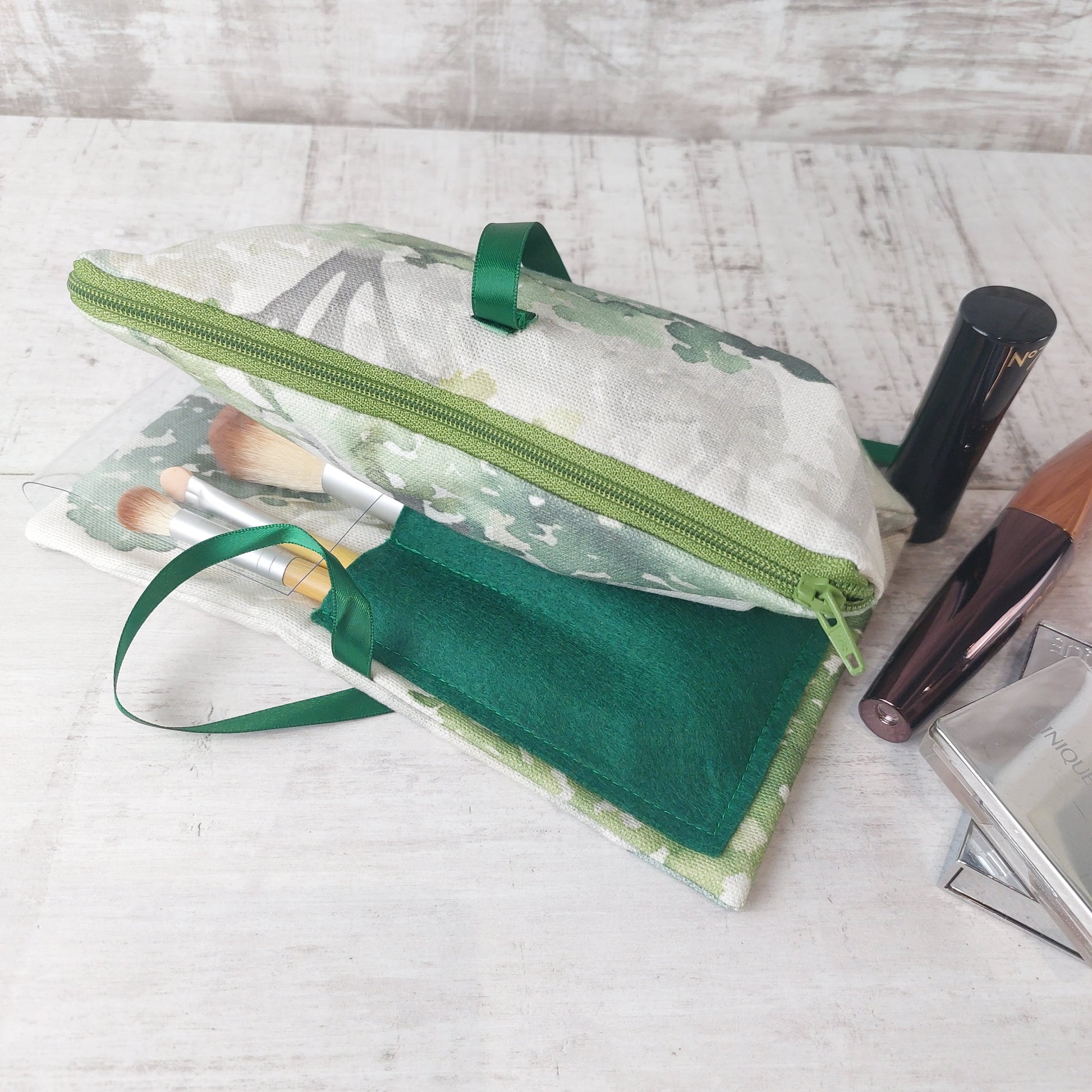 Forest green tree print makeup organiser with a green felt brushes pouch and zip compartment, pictured with makeup brushes and makeup essentials.