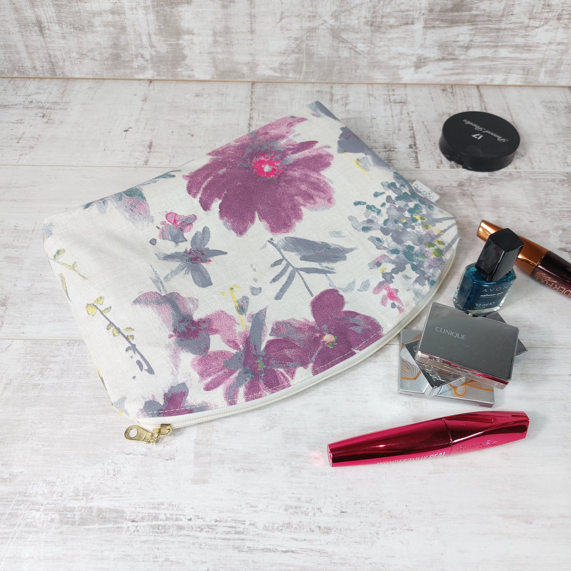 Large watercolour floral makeup bag laid next to a collection of mascara, nail varnish and other makeup essentials.