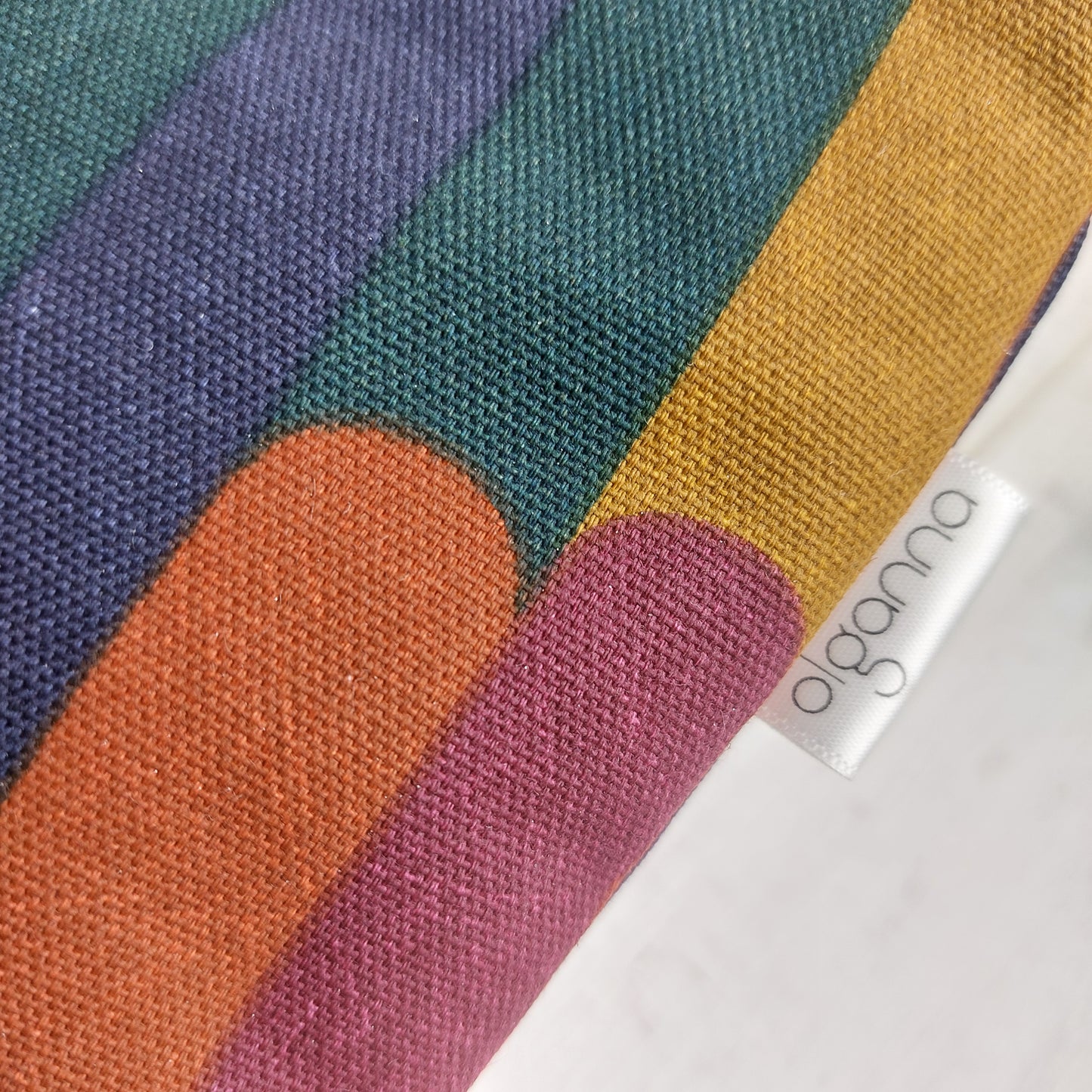Closeup of toiletries zip bag in an autumn shades stripe pattern with side label saying 'olganna'.
