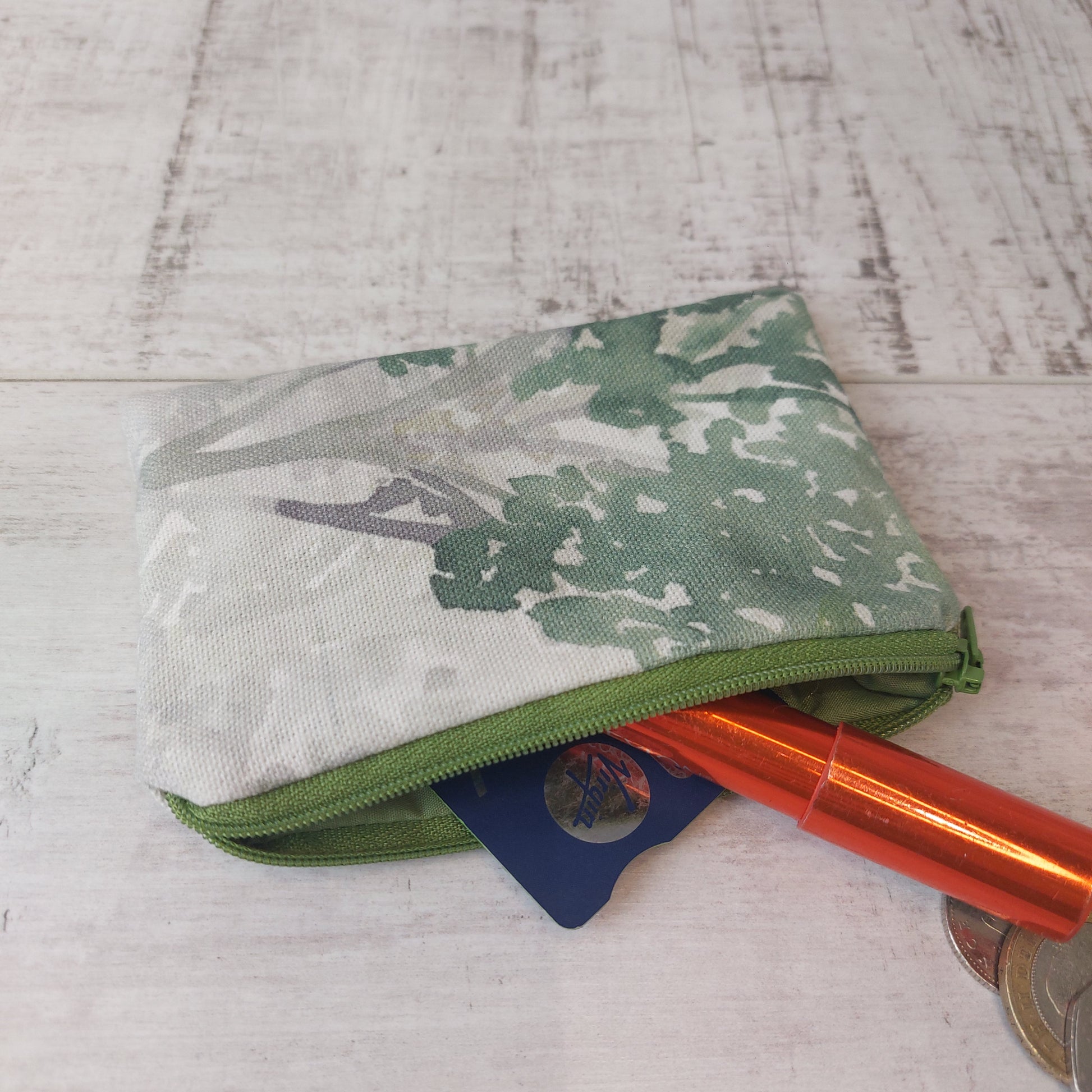 Green tree print zip purse pictured with coins, card and lipstick.