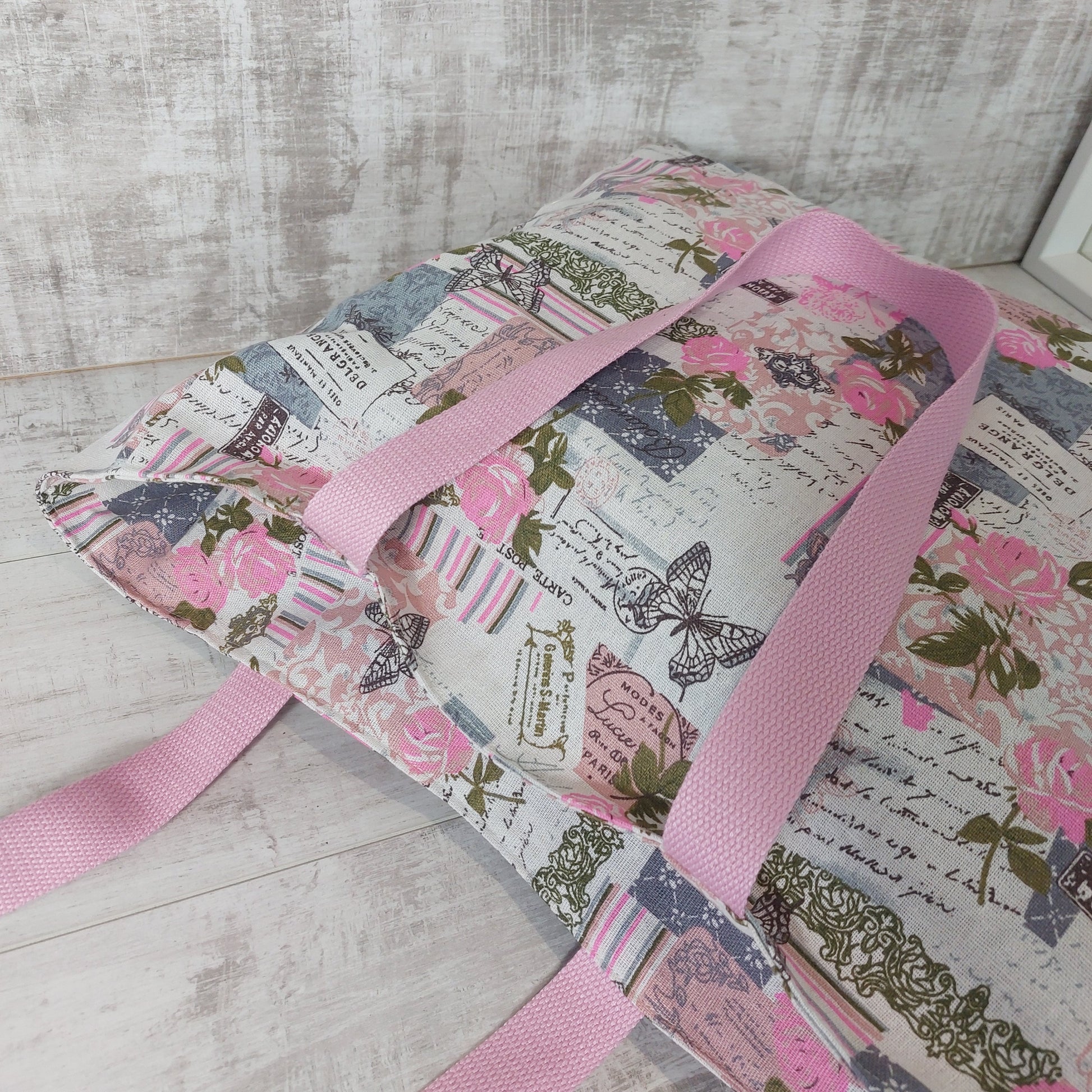 Pink and grey vintage rose and butterfly print beach bag, with deep-set zip closure, lying down. 