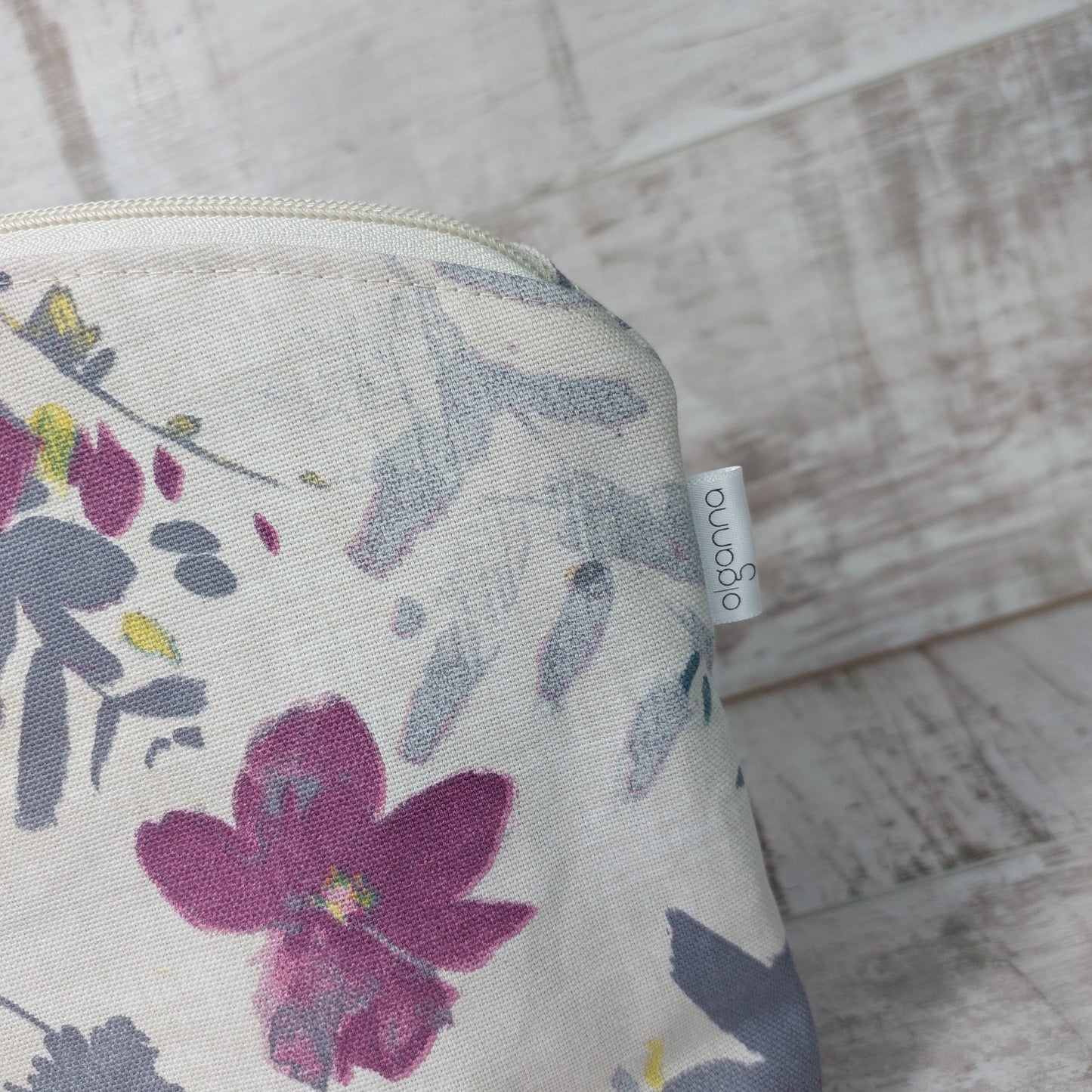 Top corner of a floral makeup bag displaying a small label stitched in the side seam, saying 'olganna'.