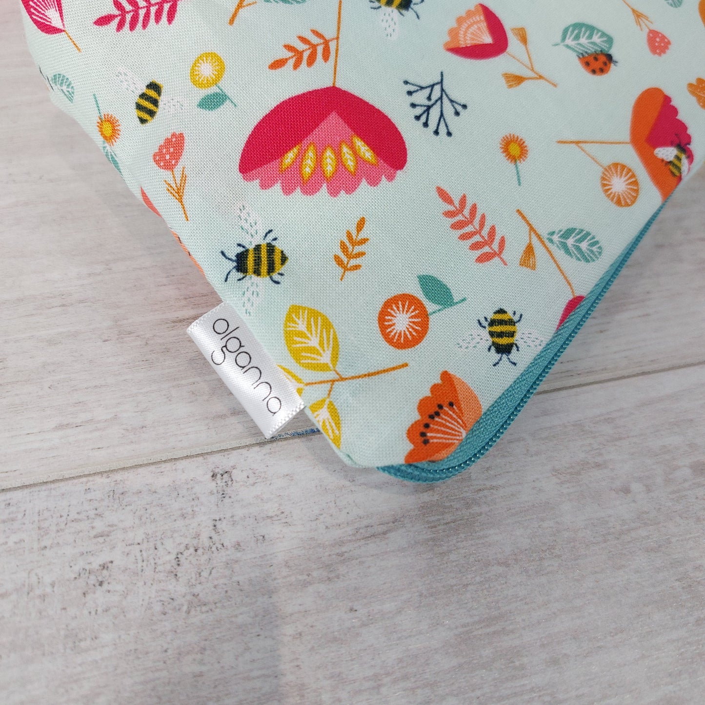 Close-up view of Spring floral and insect print makeup bag with side label saying 'olganna'. 