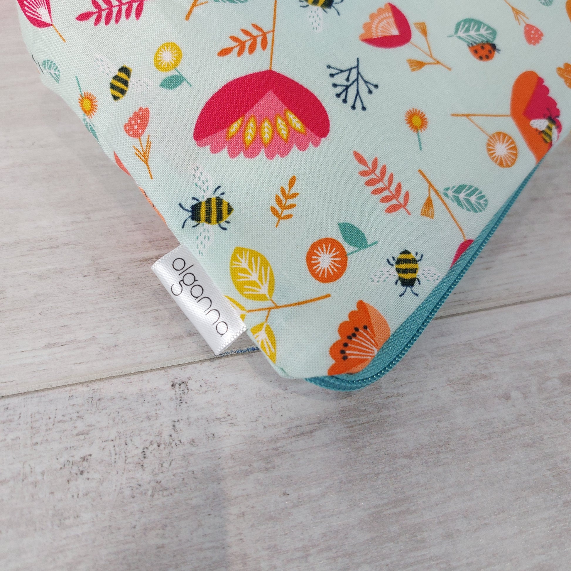Close-up view of Spring floral and insect print makeup bag with side label saying 'olganna'. 