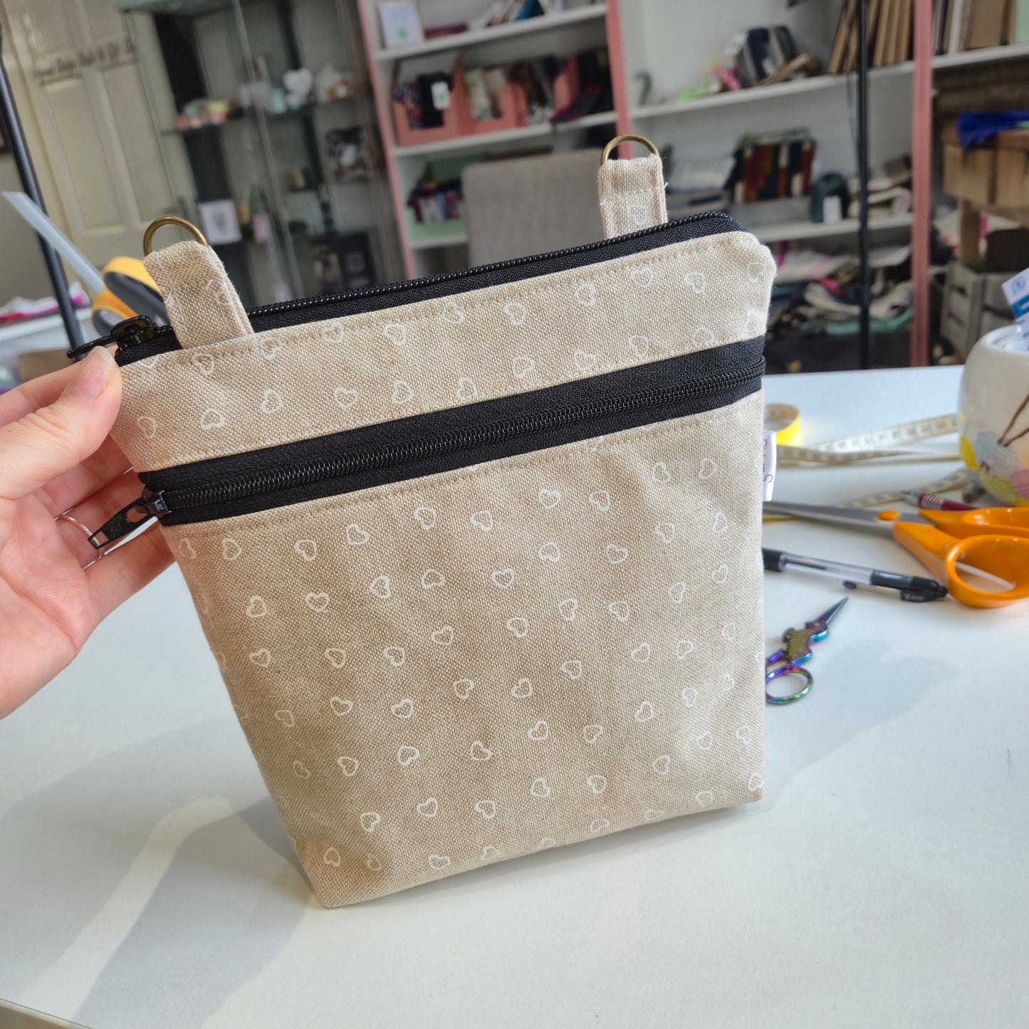 Hand holding a beige fabric pouch with black zipper in a workshop setting
