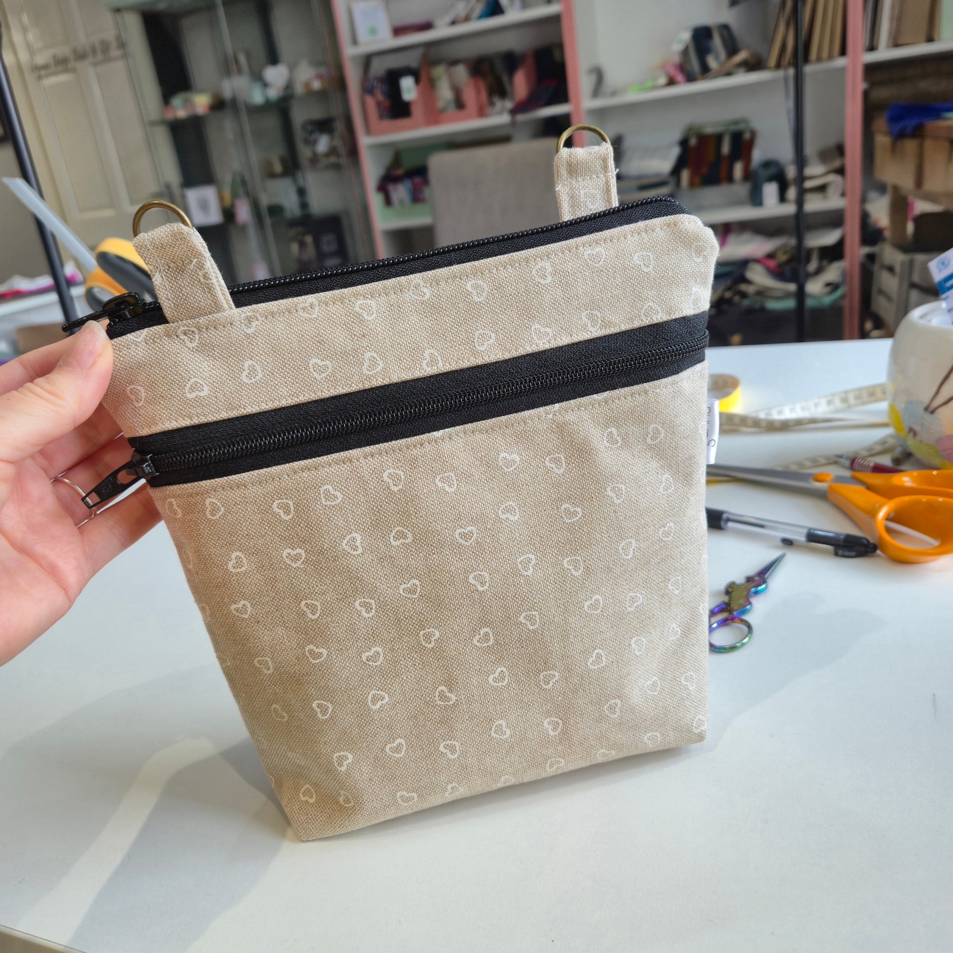 Hand holding a beige fabric pouch with black zipper in a workshop setting