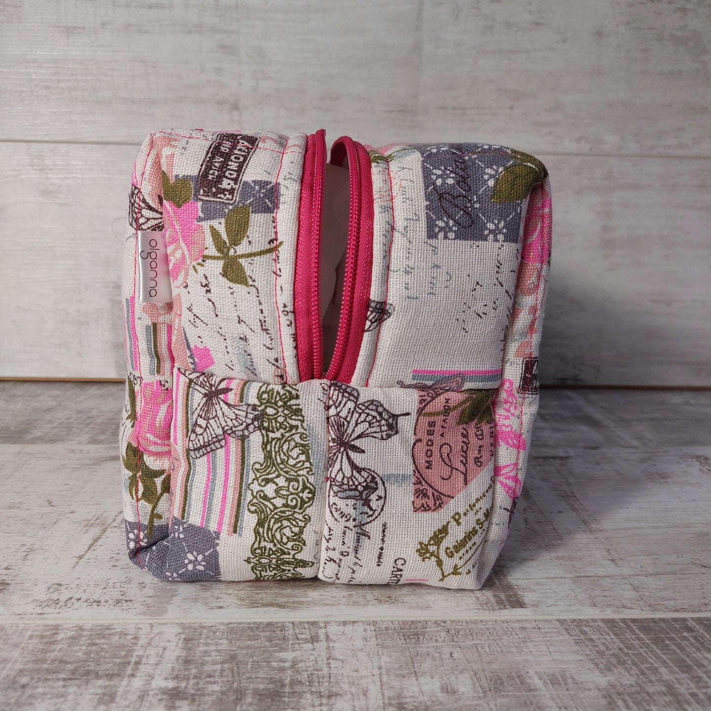 Pink and grey vintage rose and butterfly print quilted toiletries & makeup bag, end view showing dark pink zip opening.