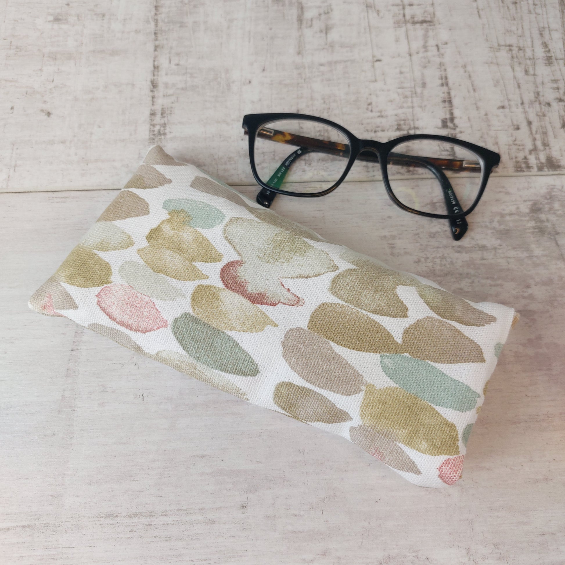 Glasses case in neutral stone pebble print, next to glasses.