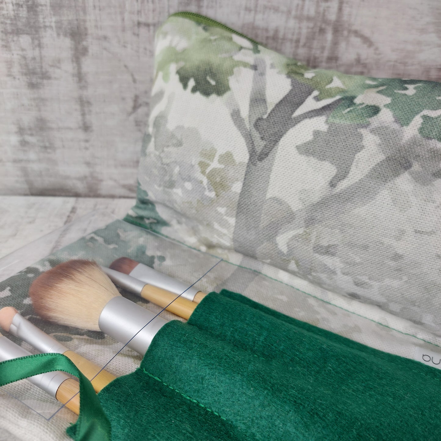 Closeup of forest green tree print makeup organiser revealing a green felt brushes pouch with a set of five bamboo-handled brushes.