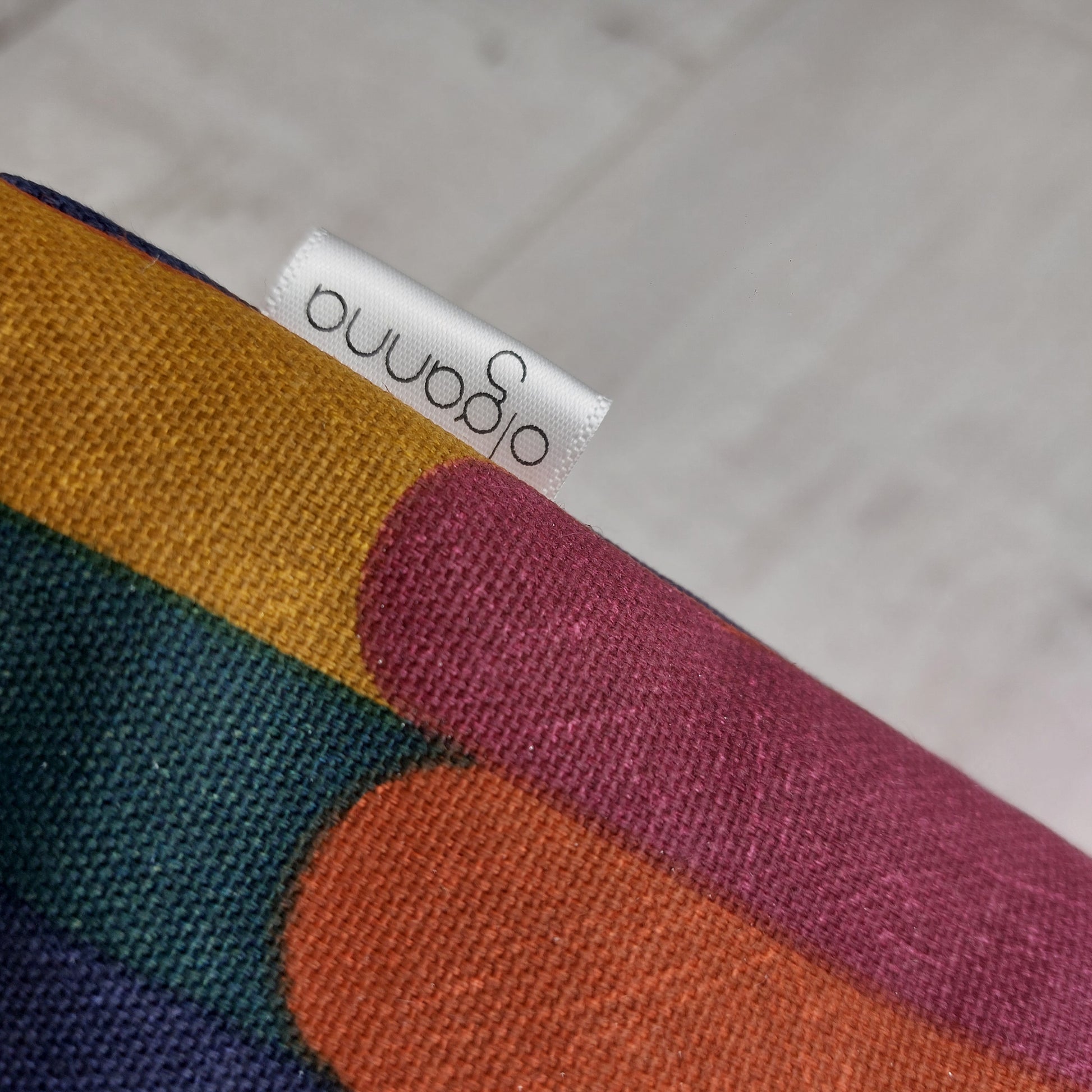 Closeup of toiletries zip bag in an autumn shades stripe pattern with side label saying 'olganna'.