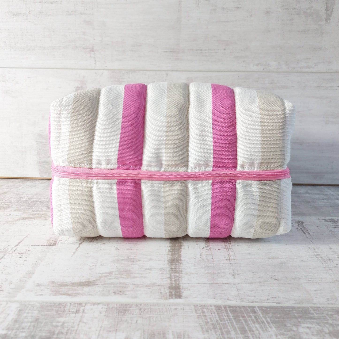 A quilted boxy bag in nautical style with pink, beige and white stripes and a pink zip, shown lying on its side.