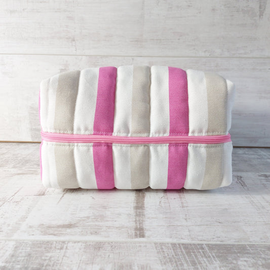 A quilted boxy bag in nautical style with pink, beige and white stripes and a pink zip, shown lying on its side.