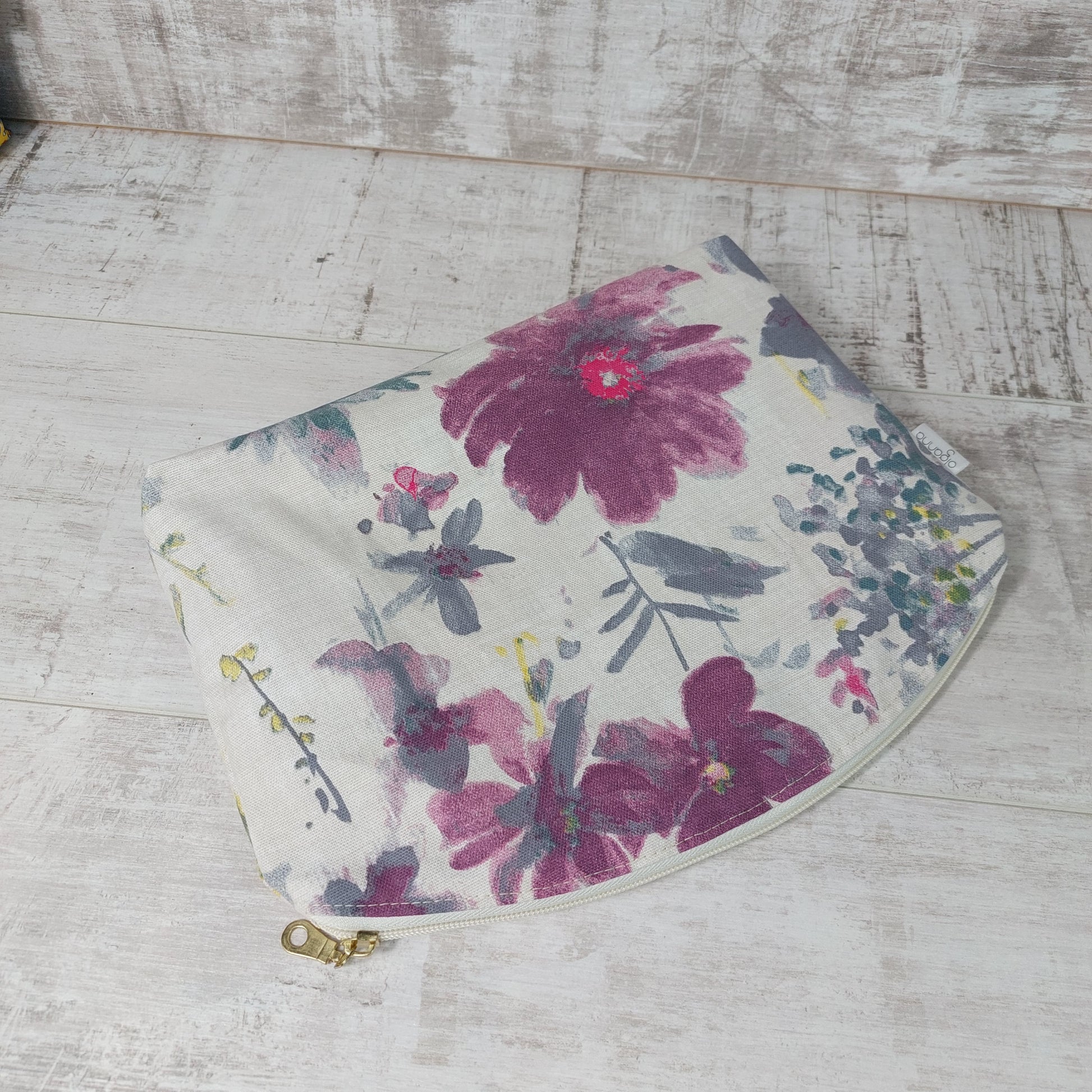 Floral makeup bag in pastel shades on a white background with zip fastening, laid on its side.