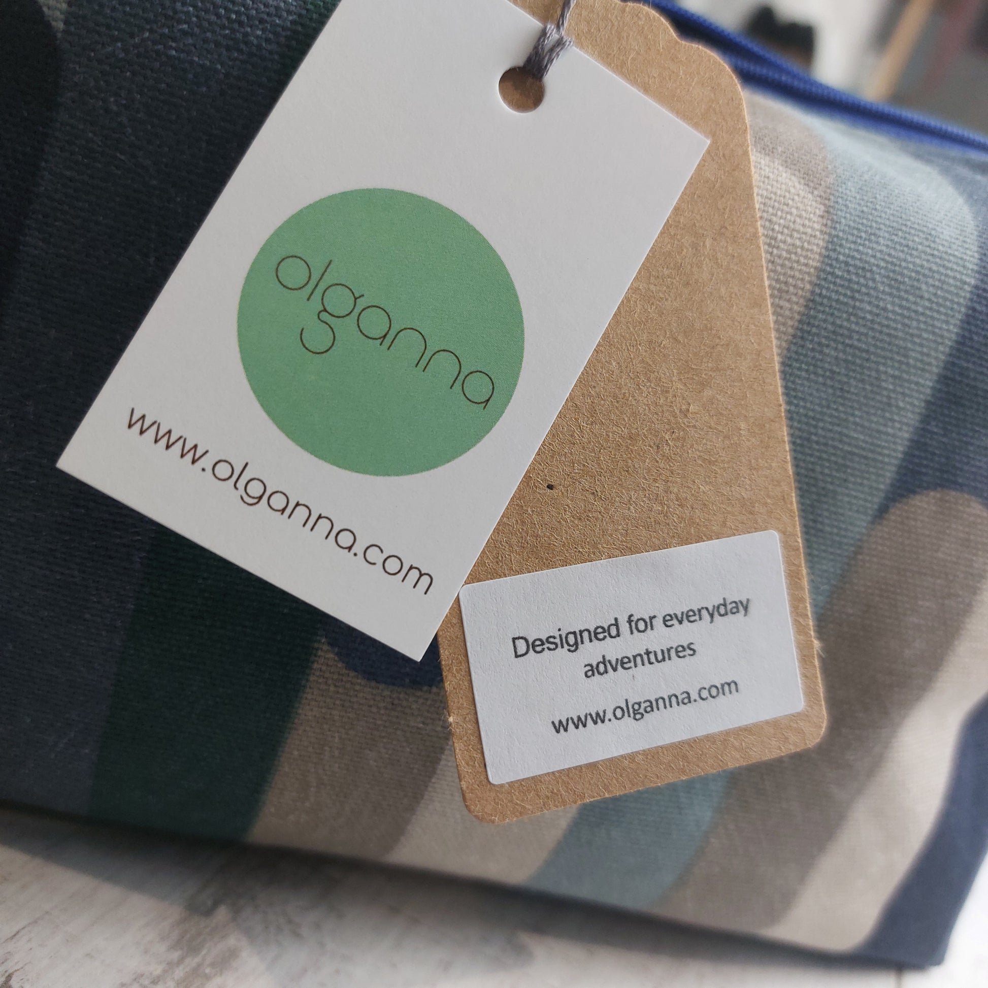 Closeup of Olganna gift tags on a boxy zip pouch in blue and winter tones with a label saying 'Designed for everyday adventures www.olganna.com'