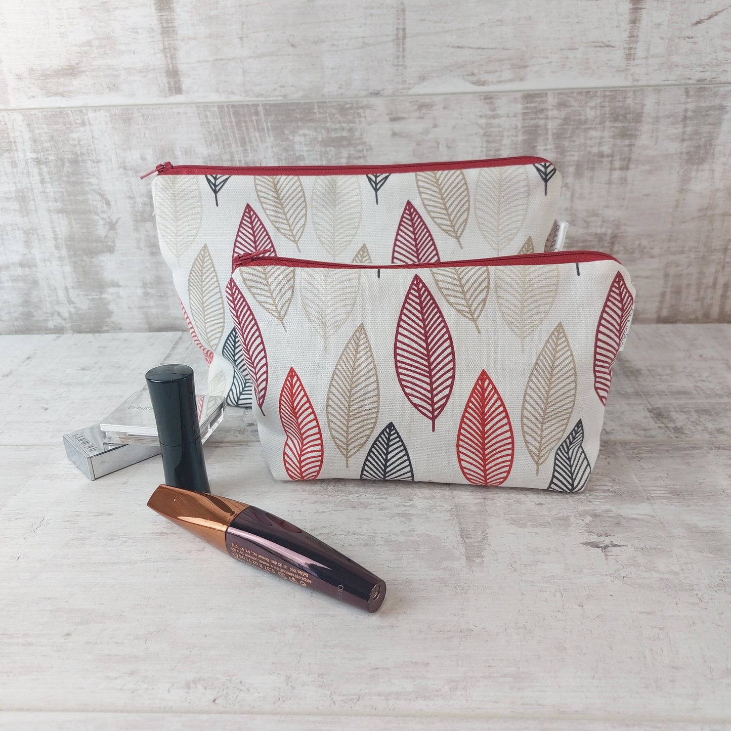 Small Scandi Autumn Leaves print pouch with larger pouch behind, pictured with beauty essentials.