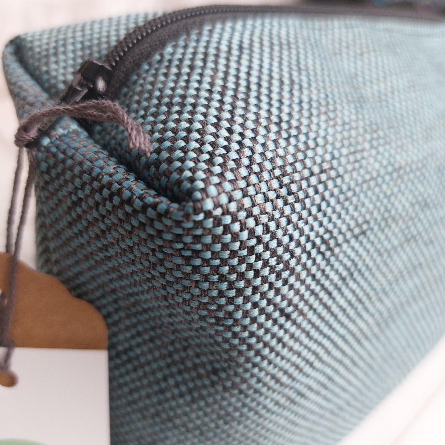 Closeup of boxy zip pouch in teal and black woven fabric showing black zip fastening.