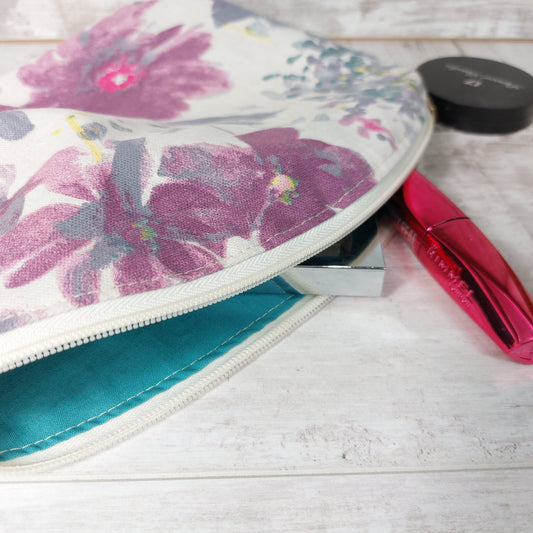 Watercolour floral makeup bag with teal lining, unzipped with makeup essentials.