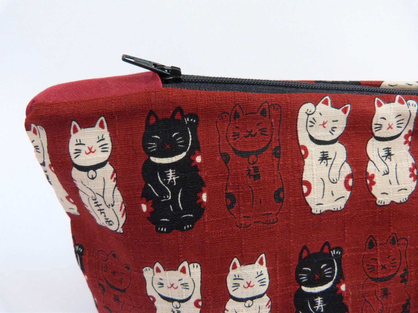 Close up of red make up bag with black zip. All overview a print of waving cats in black and cream to contrast.